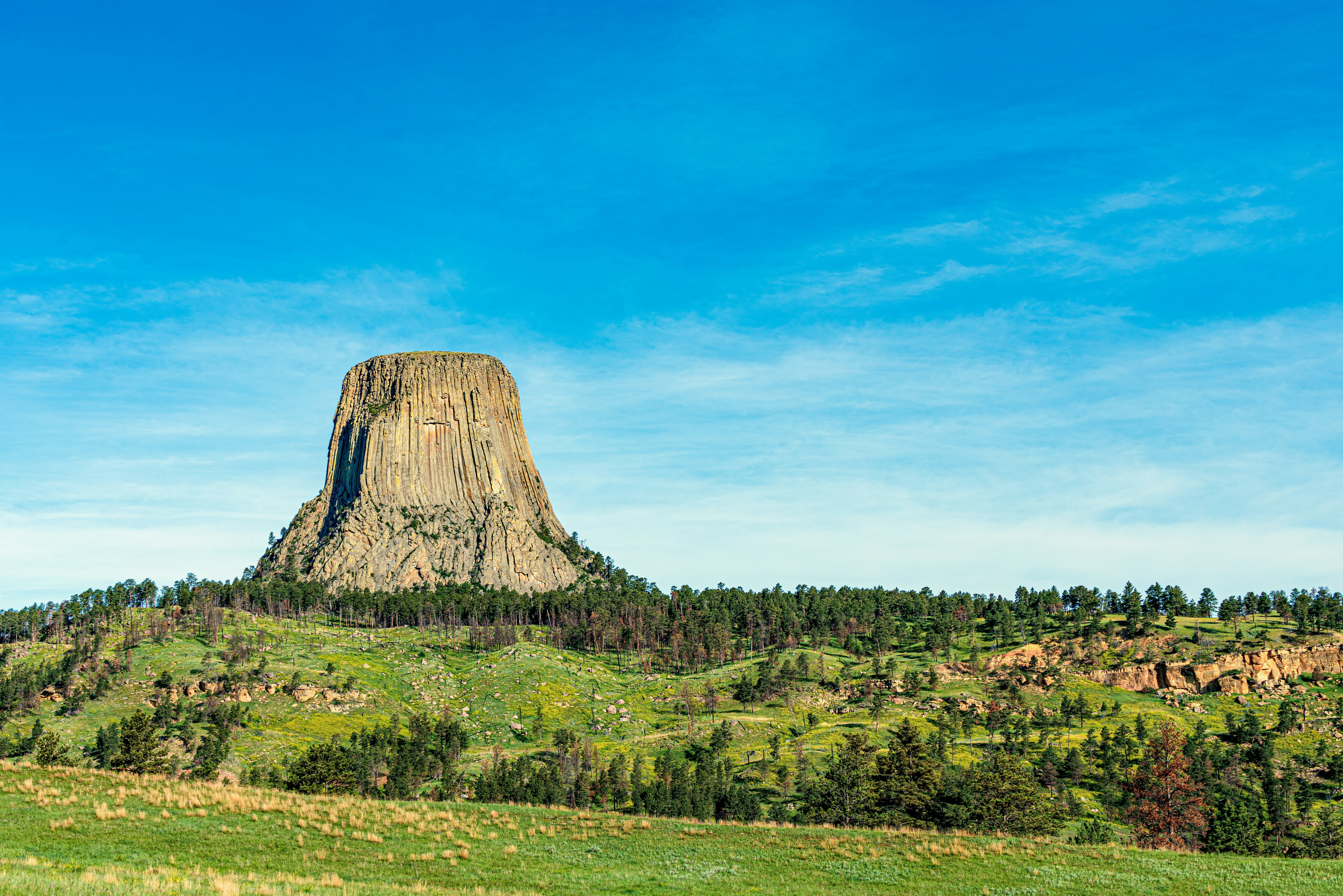 green grass field near brown rock formation under blue sky during daytime